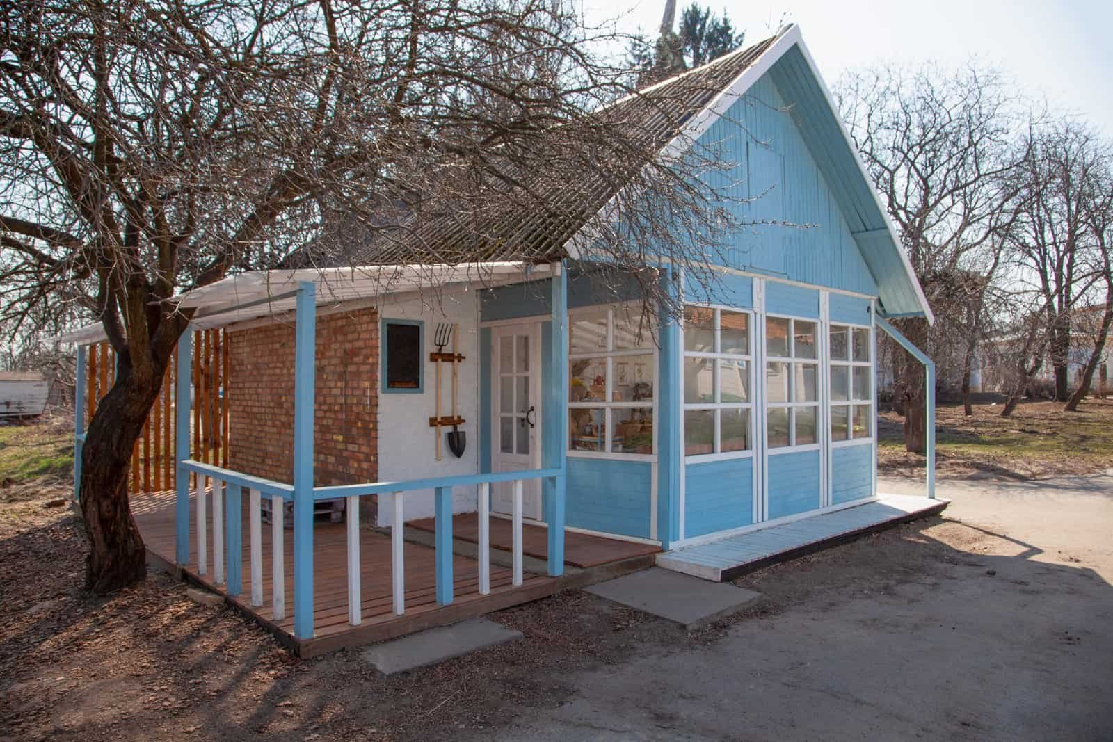 Colorful outdoor sunroom with blue paneling and brick accents, surrounded by trees; perfect for home expansion or leisure spaces.